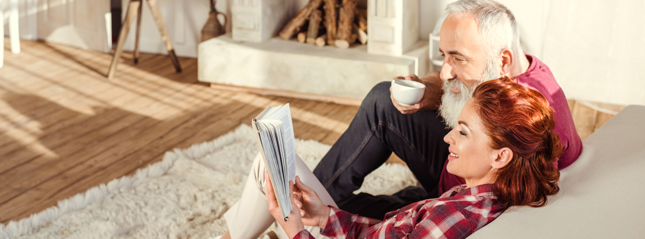 older Man and woman sitting in the couch reading a magazine