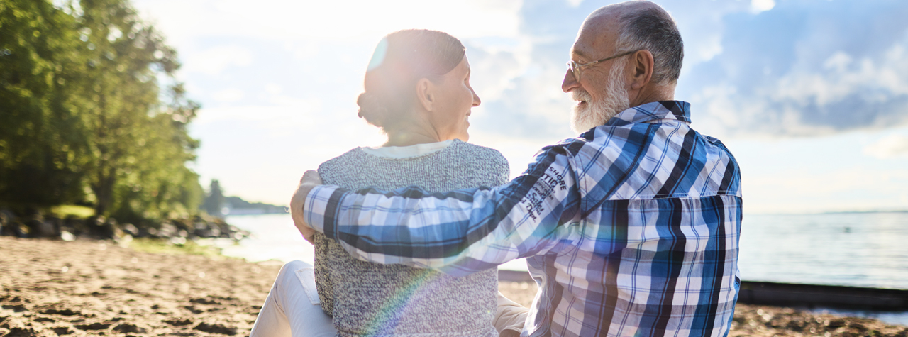 older Man puts arm around woman and smiling at the beach